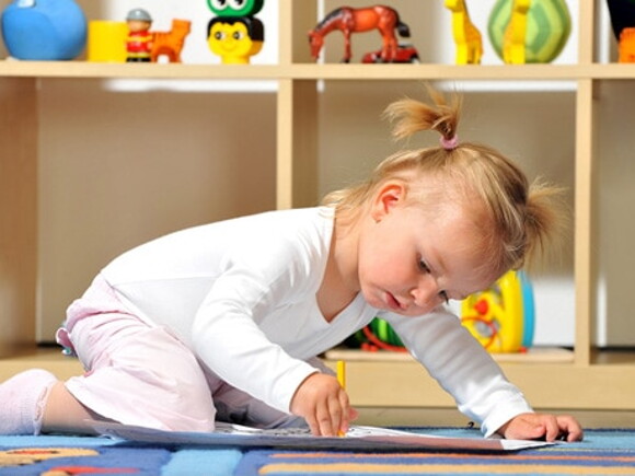 Petite fille avec des couettes est agenouillée sur le sol de sa chambre et dessine sur une feuille