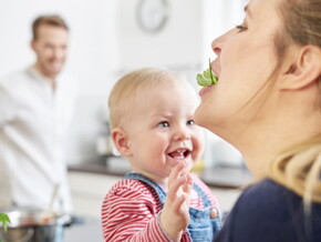 Bébé qui donne à manger à sa maman avec papa en arrière-plan