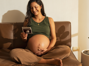 Femme enceinte assise sur un canapé tenant une échographie dans ses mains