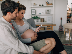 Pregnant woman and partner sitting on a couch, holding a phone.