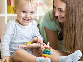 Maman est accroupi à côté de bébé qui joue assis et rigole avec lui