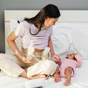 Femme assise sur un lit utilisant un tire-lait, avec un nourrisson allongé à côté.