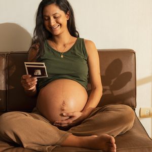 Femme enceinte assise sur un canapé tenant une échographie dans ses mains