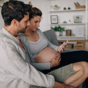 Pregnant woman and partner sitting on a couch, holding a phone.