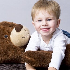 Bébé sourit à quatre pattes et grimpant au dessus d'un ours en peluche couché sur le dos