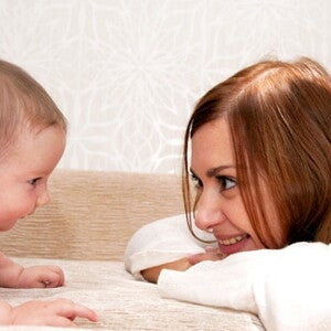 Maman est accroupie face à bébé qui rampe et sourit en le regardant