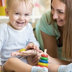 Maman est accroupi à côté de bébé qui joue assis et rigole avec lui