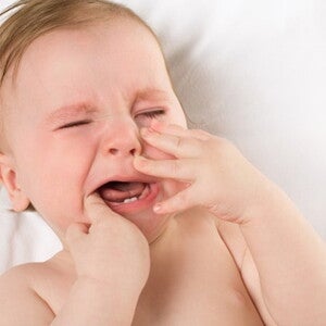 Bébé est allongé sur le dos les mains devant sa bouche et pleure fortement