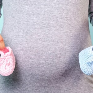 Ventre de maman avec des chaussons rose et bleu dans les mains