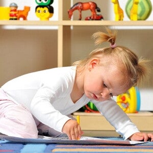 Petite fille avec des couettes est agenouillée sur le sol de sa chambre et dessine sur une feuille