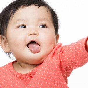 Bébé assis avec un pull rose lève le bras gauche et bouge ses doigts