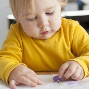 Bébé avec pull jaune assis à un bureau dessine