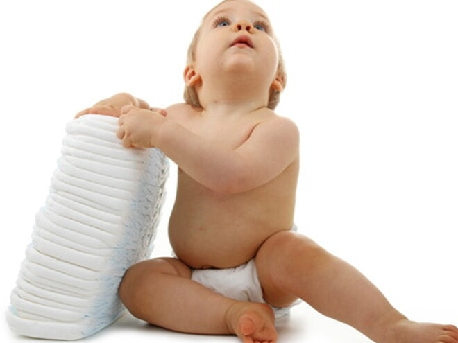 Bébé avec une couche est assis regardant en l'air et tient un paquet de couches se trouvant à sa droite