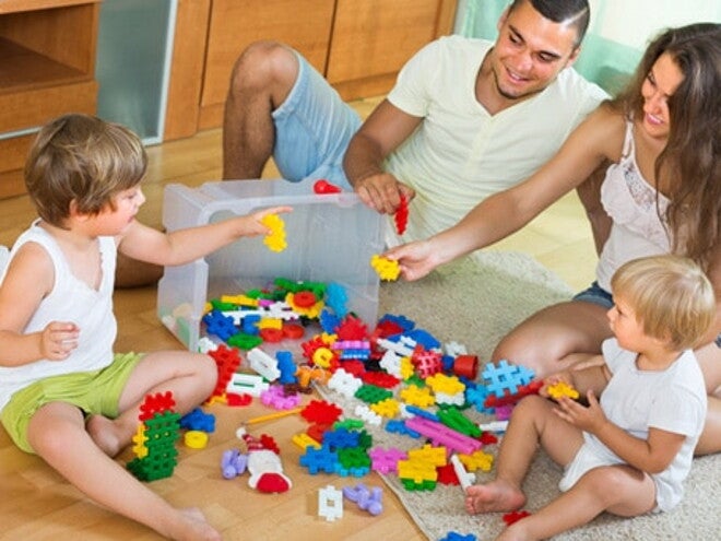 Papa et maman jouent aux jeux de construction avec leurs deux enfants à même le sol