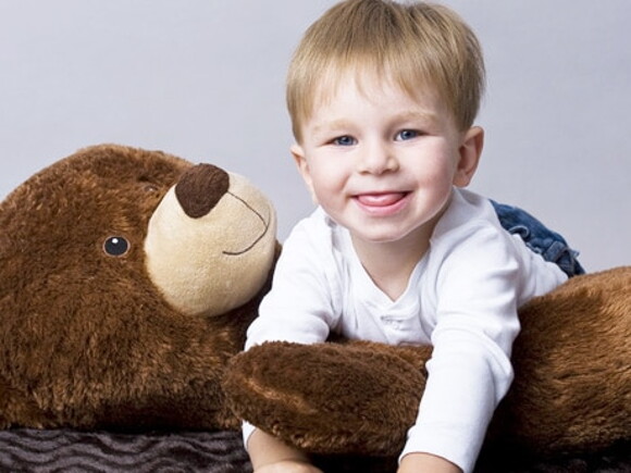 Bébé sourit à quatre pattes et grimpant au dessus d'un ours en peluche couché sur le dos