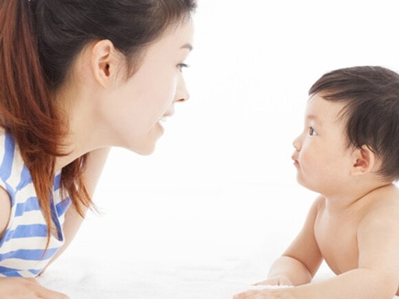 Maman est accroupie face à bébé et lui parle en articulant pour lui apprendre le langage