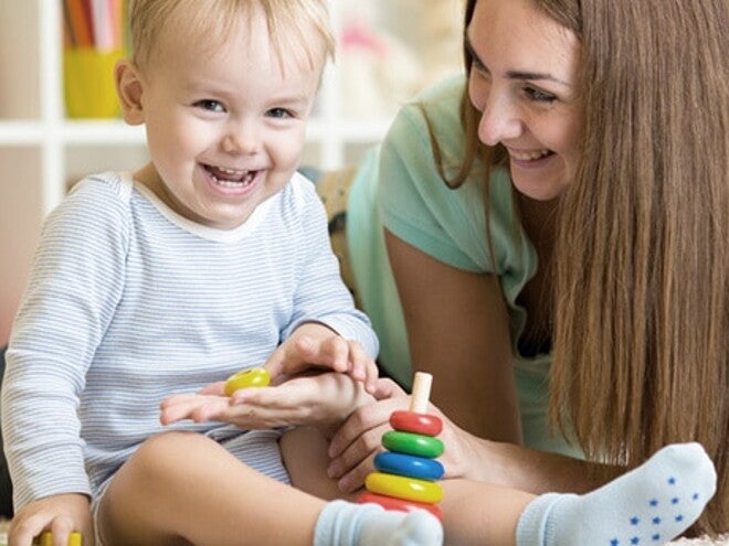 Maman est accroupi à côté de bébé qui joue assis et rigole avec lui Maman est accroupi à côté de bébé qui joue assis et rigole avec lui