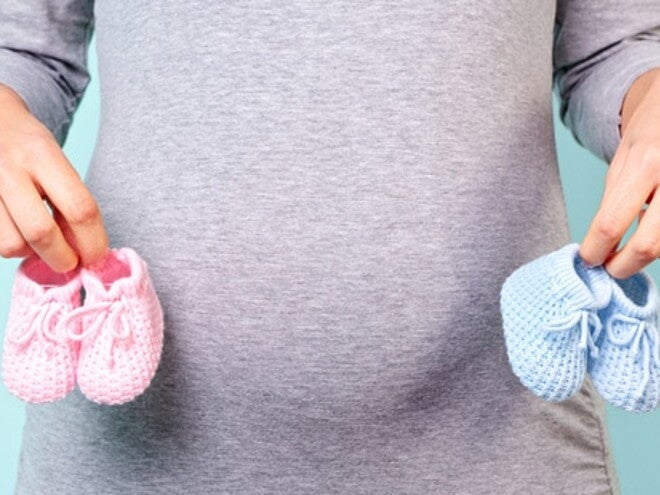 Ventre de maman avec des chaussons rose et bleu dans les mains